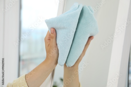 Woman cleaning mirror with rag indoors, closeup