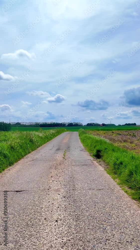 A beautiful country road surrounded by lush green fields under a bright blue sky with fluffy clouds. A beautiful country road surrounded by lush green fields under a bright blue sky with fluffy clouds.