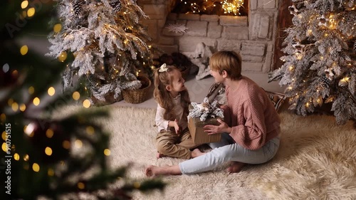 Charming young mother and daughter 5-6 years old in casual clothes, in a cozy and decorated Christmas living room at home against the backdrop of the Christmas tree.