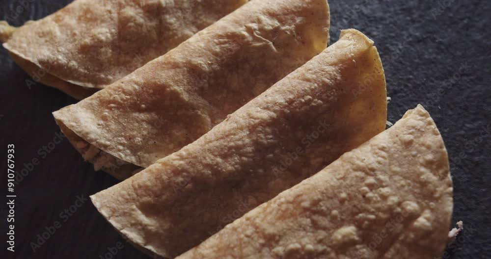 Beautiful slow motion shot of a group of 4 tacos or Mexican tortillas with chicken placed on a black plate and dimly lit. It is a close-up with smooth and continuous movement on the tortillas.