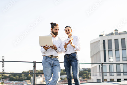 Fotografija Young man and woman standing outdoors discussing work on laptop and smartphone