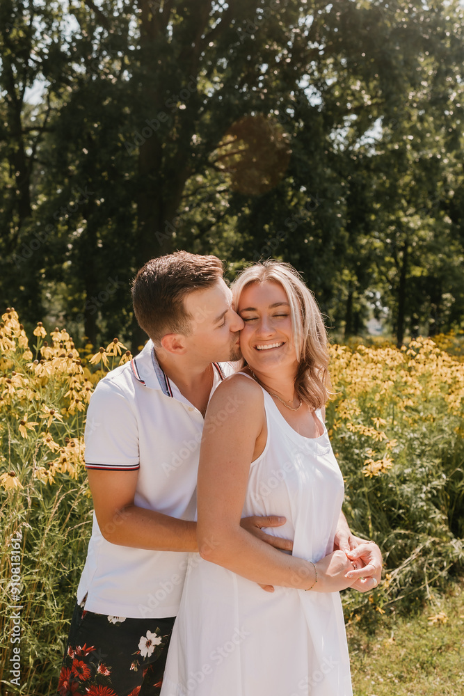Fototapeta premium Young couple embracing and smiling in front of wildflowers