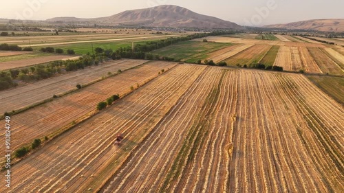 Drone video of the tractor working in the field forming hay into briquettes in sunset time. Harvesting time. Amazing agricultural landscape with fields and nountains photo