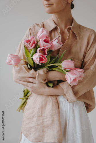 Person in Light Beige Shirt and White Skirt Holding a Bouquet of Pink Tulips Against Neutral Background. Close-Up of Flowers and Upper Body for Floral and Fashion Aesthetics photo