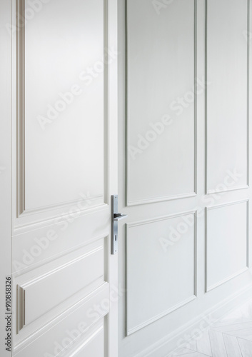 Fotografie A modern white door partially open in a bright, airy room featuring stylish paneling and minimal decor