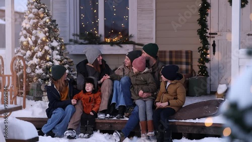 A large family in winter clothes and sweaters poses on the porch of a private country house on Christmas Day against the backdrop of the Christmas tree. The concept of holiday and togetherness.