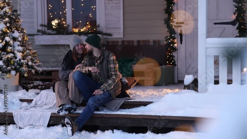 A family in winter clothes and sweaters poses on the porch of a private country house on Christmas Day against the backdrop of the Christmas tree. The concept of holiday and togetherness.