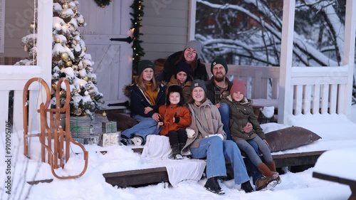 A large family in winter clothes and sweaters poses on the porch of a private country house on Christmas Day against the backdrop of the Christmas tree. The concept of holiday and togetherness.