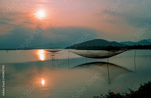 Eingescanntes Diapositiv einer historischen Farbaufnahme von Fischernetzen über einem See in der Abenddämmerung mit Sonnenuntergang in Zentralvietnam photo