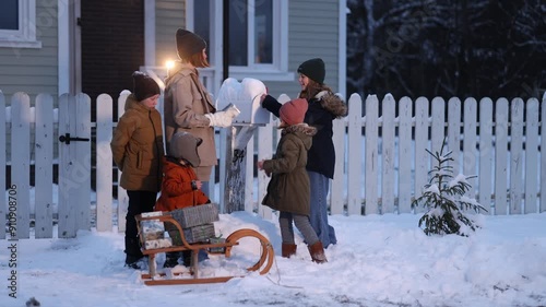 Children stack Christmas gifts in a sleigh in the backyard of a ranch-style house in winter. The concept of preparing for a Happy New Year and Christmas.