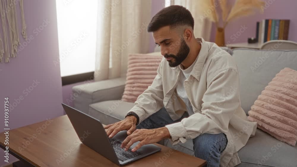 Young hispanic man working on a laptop in a well-decorated living room with soft lighting and pastel-colored cushions, creating a cozy home environment. Young hispanic man working on a laptop in a well-decorated living room with soft lighting and pastel-colored cushions, creating a cozy home environment.