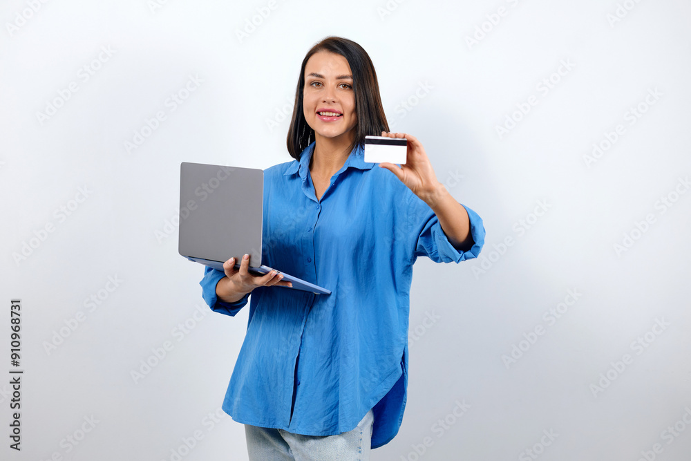 Cute brunette woman dressed in a stylish blue shirt works using a computer and holds a poster card with a mockup Cute brunette woman dressed in a stylish blue shirt works using a computer and holds a poster card with a mockup