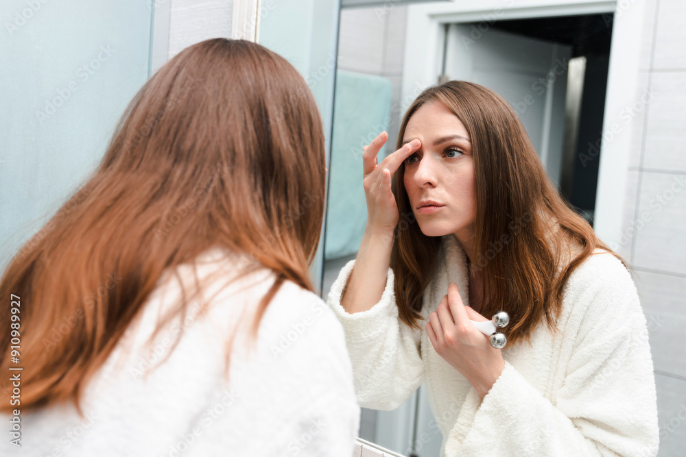 A young woman holds a facial massager in her hands. A model in a white bathrobe. Home skin care A young woman holds a facial massager in her hands. A model in a white bathrobe. Home skin care