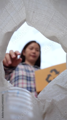 Asian woman holds a box that sorting the garbage for separate trash for recycle and reuse, throws a plastic bottle into a trash bag. sustainability concepts. vertical footage