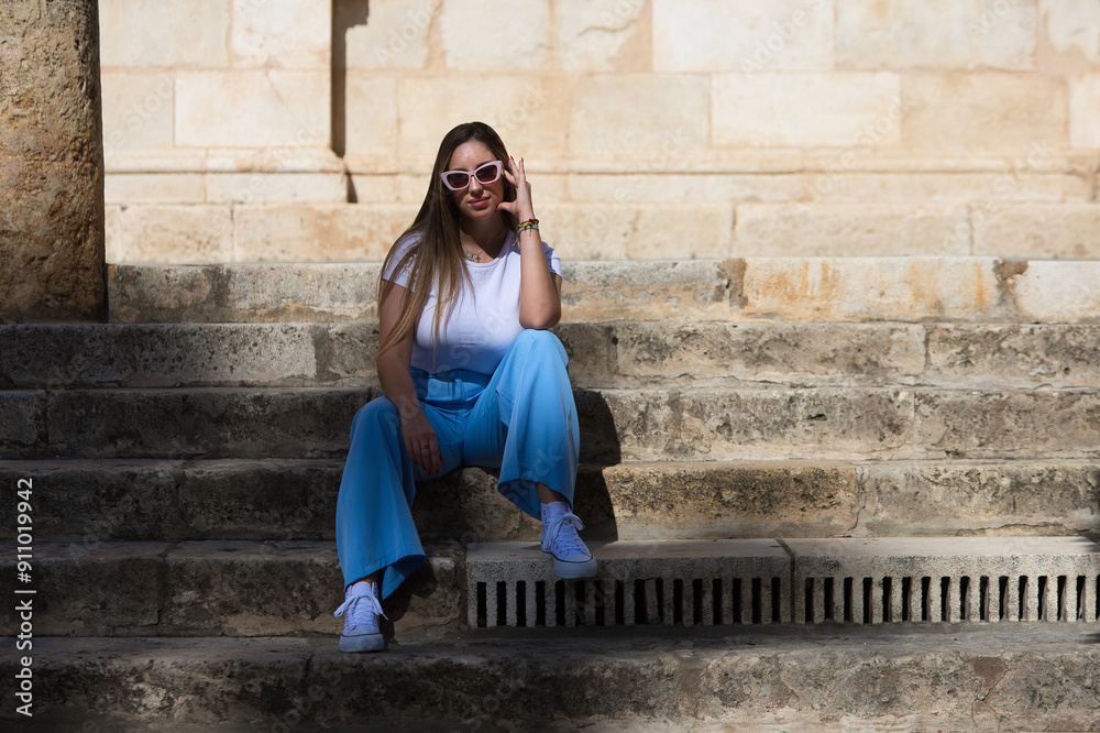 Young beautiful woman dressed in jeans, white t-shirt and sunglasses sitting on the steps of an old building in the centre of Seville. The woman is happy and having fun while doing body postures. Young beautiful woman dressed in jeans, white t-shirt and sunglasses sitting on the steps of an old building in the centre of Seville. The woman is happy and having fun while doing body postures.