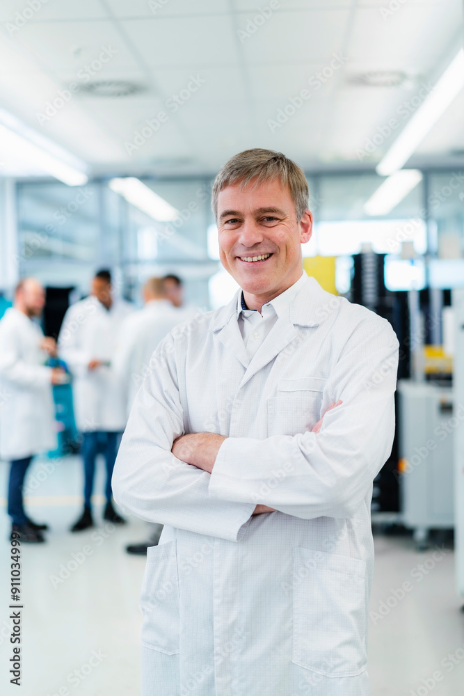 Technician in white lab coat standing in electronics factory with arms crossed Technician in white lab coat standing in electronics factory with arms crossed