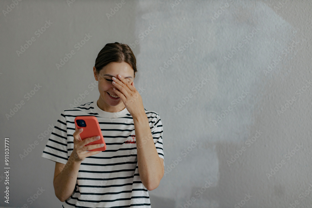 Smiling woman holding smart phone and standing in front of white wall Smiling woman holding smart phone and standing in front of white wall