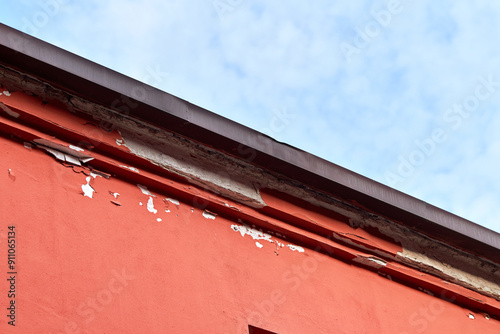 Cracked red paint peeling off, damaged plaster on facade of building. Building wall with damaged plaster and peeling paint. Defect due to unskilled workers. photo