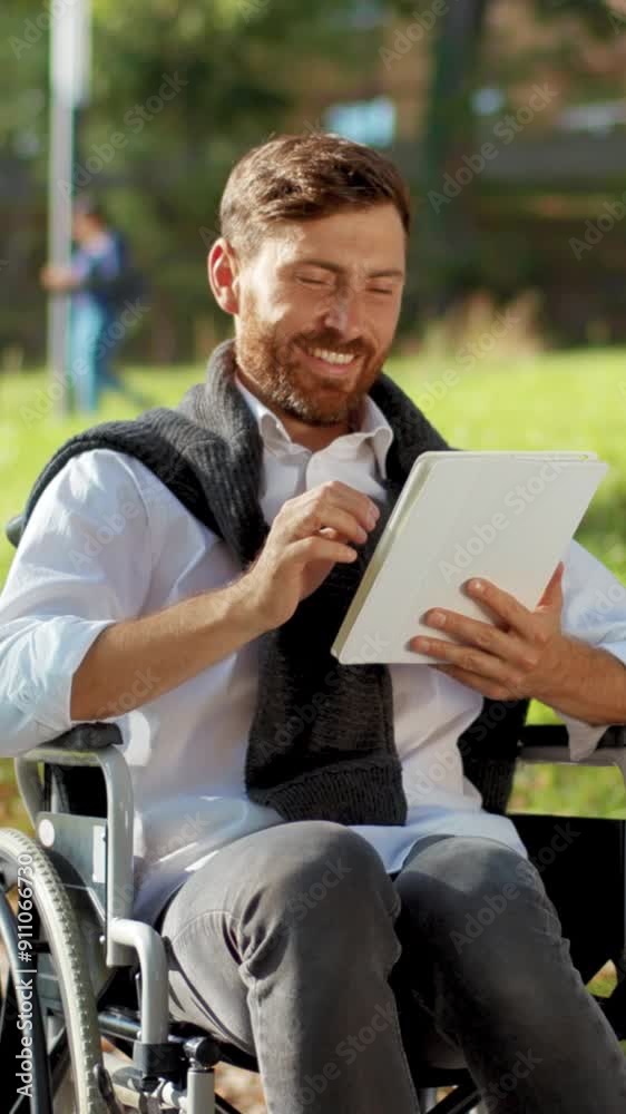 Smiling young man on a wheelchair with tablet computer in park at sunlight disability medicine. Possibility handicapped handicap tablet internet. Slow motion Smiling young man on a wheelchair with tablet computer in park at sunlight disability medicine. Possibility handicapped handicap tablet internet. Slow motion