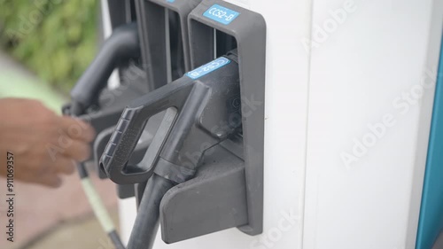 Close-up of plugging and unplugging an electric car charger at a charging station. Shows interaction with the charging port, unplugging process, and closing the car's charging flap