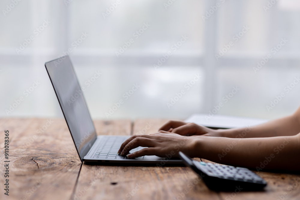 Close up of female hands while typing on laptop use calculator accountant Close up of female hands while typing on laptop use calculator accountant
