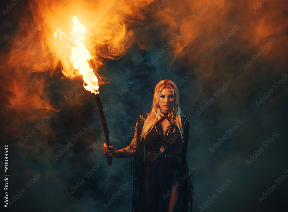 Obraz premium Gothic fantasy woman walking in mystical dark foggy forest holding burning torch in hands, bright fire flame lights way in darkness. Sexy Girl witch in black long boho style dress beauty fairy face