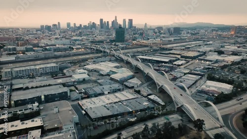 A drone shot of the Ribbon Of Light 6th Street Bridge during sunset in Los Angeles California with cars driving in the foreground of the city's skyline from about 300 feet above the ground