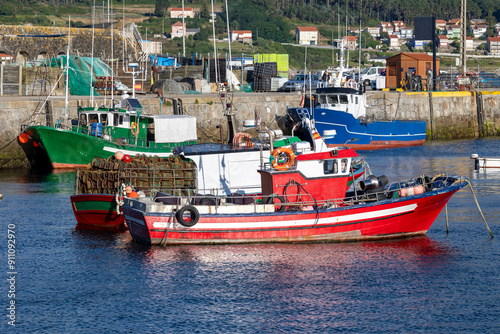 Фотография A picturesque scene of colorful fishing boats moored in a tranquil marina harbor, with a backdrop of a quaint coastal village and lush green hills under clear blue skies