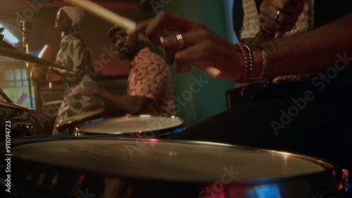 Close up view of hands of unrecognisable male drummer performing with two bandmates playing guiro and conga during concert in bar photo