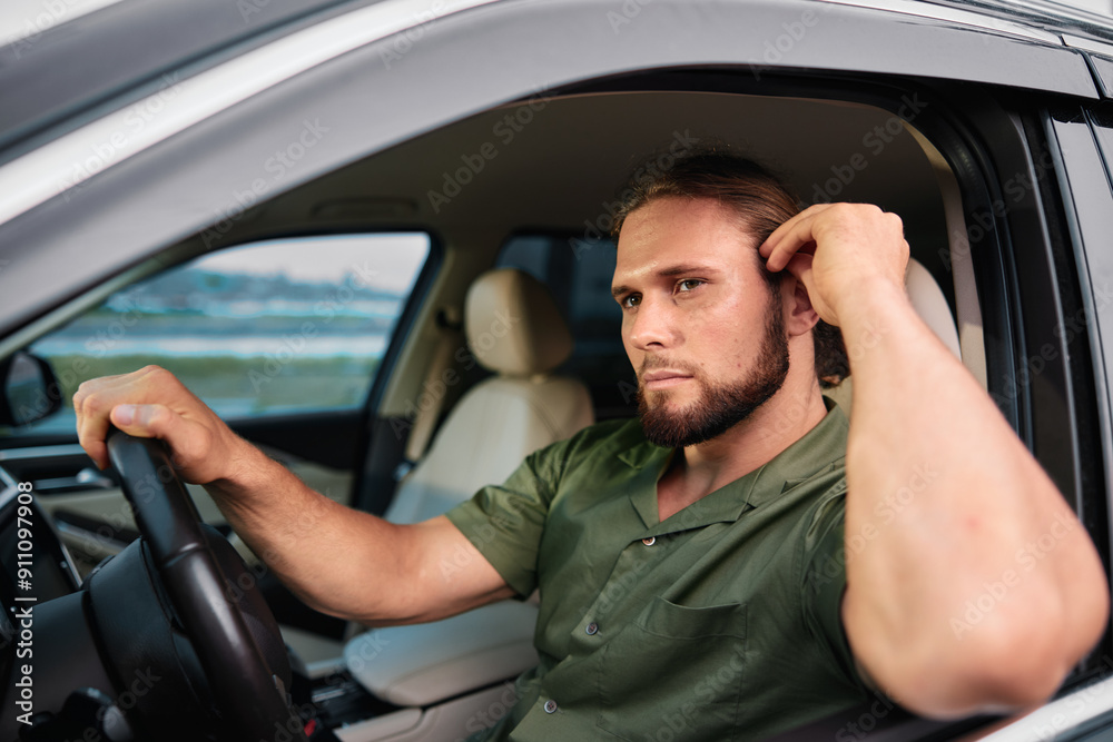 Thoughtful man sitting in a car, looking out with a serious expression Thoughtful man sitting in a car, looking out with a serious expression