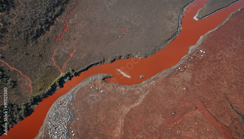 Aerial view showcasing a striking contrast between red river water and dry, earthy landscape, perfect for environmental themes, nature documentaries, or climate discussions.