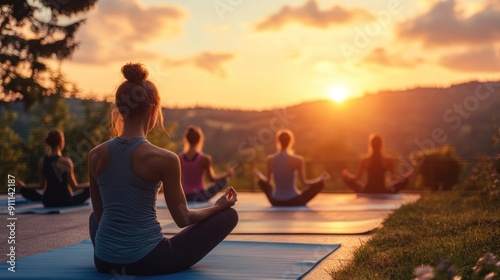 Group of people practicing yoga outdoors on mats with a scenic sunset background