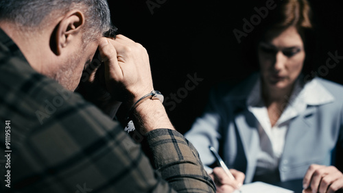 Female police detective questioning a man in handcuffs, suspect crying, confession