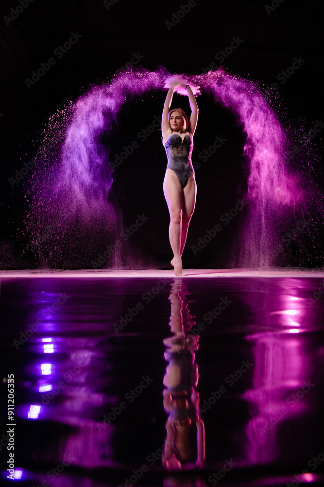 Young slim woman posing near mirror surface with purple particles sprayed in the air
