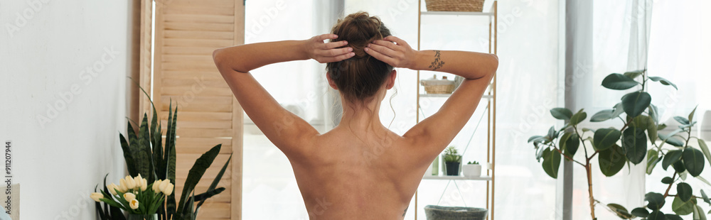 Naklejka premium A confident young woman adjusts her hair in a stylish indoor setting.