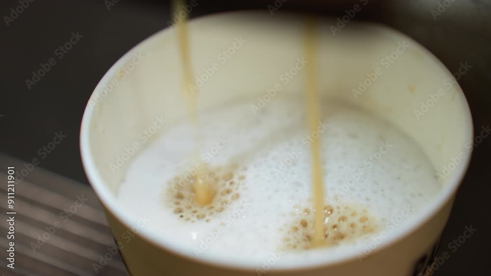 coffee pouring into a cup from a coffee machine. The video captures the detailed view of the coffee stream blending with the frothy milk in the cup coffee pouring into a cup from a coffee machine. The video captures the detailed view of the coffee stream blending with the frothy milk in the cup