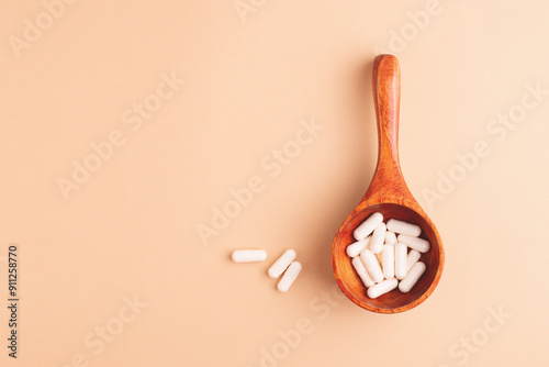 Wooden spoon with white capsules on beige background, top view. Dietary supplements and natural remedies in a simple, elegant composition.