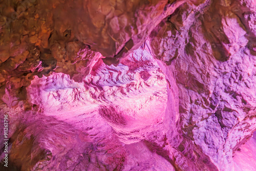 Tunnel in an underground rock formation illuminated with artificial purple-pink light, cracked, rough and uneven walls due to water seepage in Neptune Caves, Couvin, Wallonia, Belgium