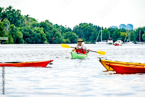 Photography kayaker (middle aged south asian man with sun hat and beard) paddling towards camera with yellow bladed paddle green kayak and red pfd shot toronto islands room for text
