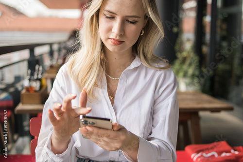 Restaurant and smartphone. Close-up relaxed blond woman typing and scroll or check email and contact social media app or social network user. Happy smile and young gen z girl with mobile tech post to