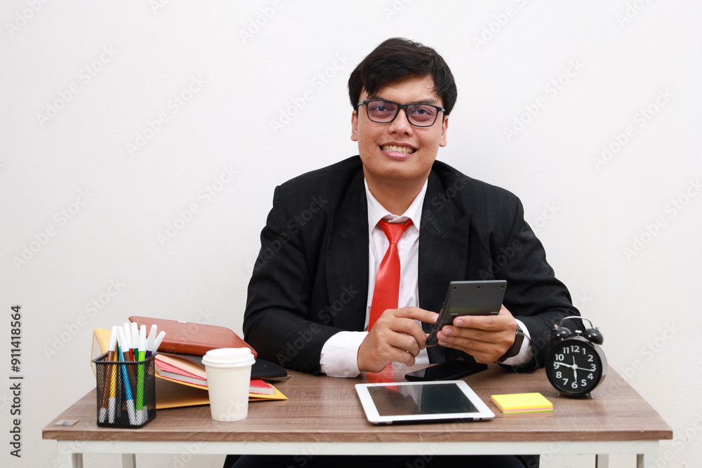 Young fun successful happy employee businessman sit work at office desk with tablet computer use calculator write isolated on white background. Achievement career concept Young fun successful happy employee businessman sit work at office desk with tablet computer use calculator write isolated on white background. Achievement career concept