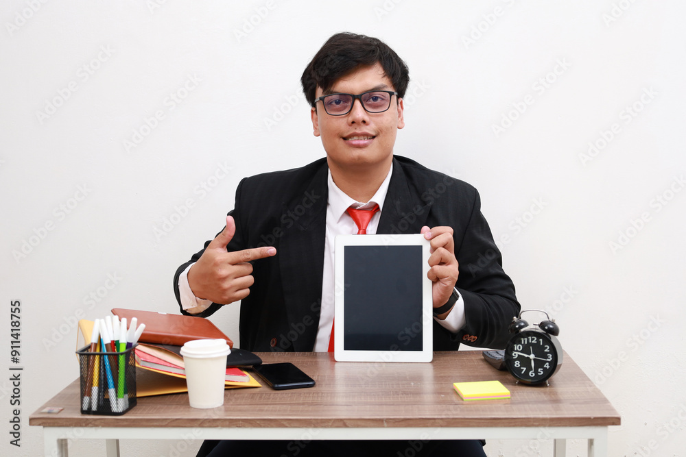 Happy Smiling Asian Businessman Sitting At Desk Showing Tablet Computer Pointing Finger At Blank Black Screen At Office For Mock Up Template, Free Copy Space. People And Technology Concept Happy Smiling Asian Businessman Sitting At Desk Showing Tablet Computer Pointing Finger At Blank Black Screen At Office For Mock Up Template, Free Copy Space. People And Technology Concept