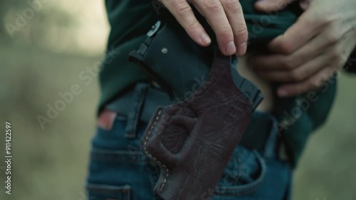 A close view of a man holstering a handgun, the scene focuses on the hands, holster, and part of the jeans as he walks away, with a blur surrounding