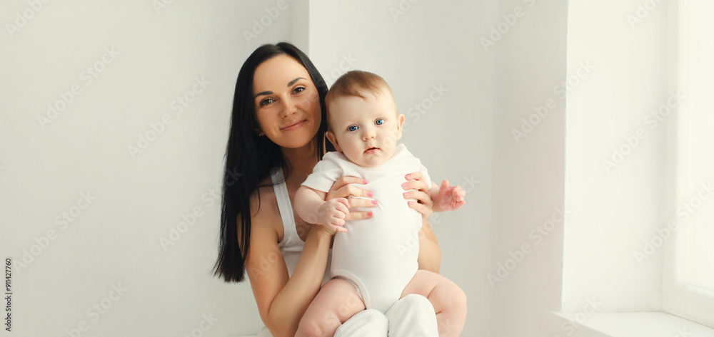 Happy smiling young mother playing with baby in white room at home Happy smiling young mother playing with baby in white room at home