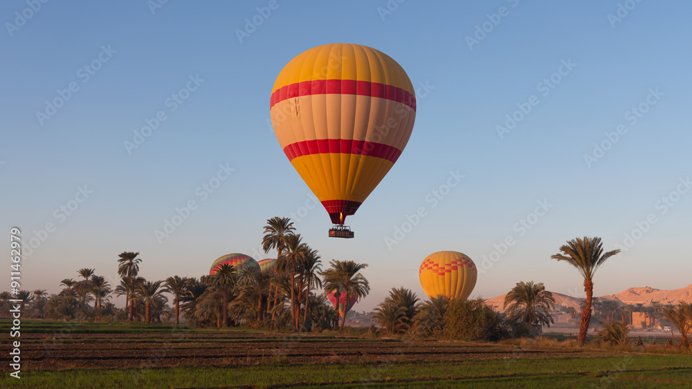 Obraz premium Hot air balloon is inflating before liftoff - Hatshepsut Temple at sunrise in Valley of the Kings and red cliffs western bank of Nile river- Luxor- Egypt