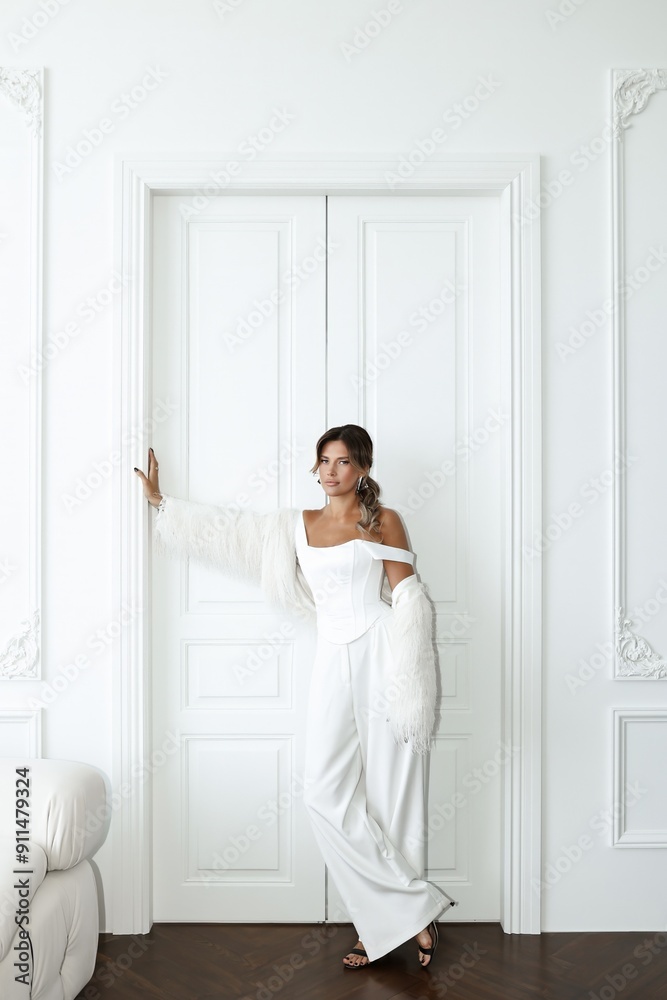 Stylish young woman with long dark hair models a white suit in a bright white room. Contemporary fashion shoot with minimalist aesthetics Stylish young woman with long dark hair models a white suit in a bright white room. Contemporary fashion shoot with minimalist aesthetics