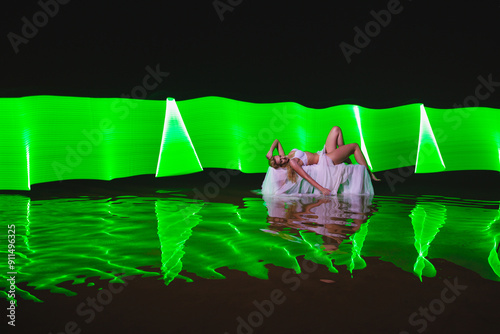 Obraz na płótnie Young slim girl in white swimsuit posing in water at night with abstract green light effect w salonie