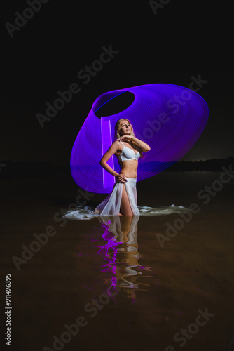 Obraz na płótnie Young slim girl in white swimsuit posing in water at night with abstract purple light effect w salonie
