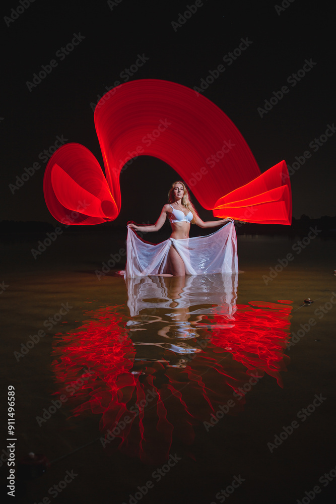 Young slim girl in white swimsuit posing in water at night with abstract red light effect