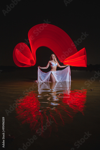 Obraz na płótnie Young slim girl in white swimsuit posing in water at night with abstract red light effect w salonie